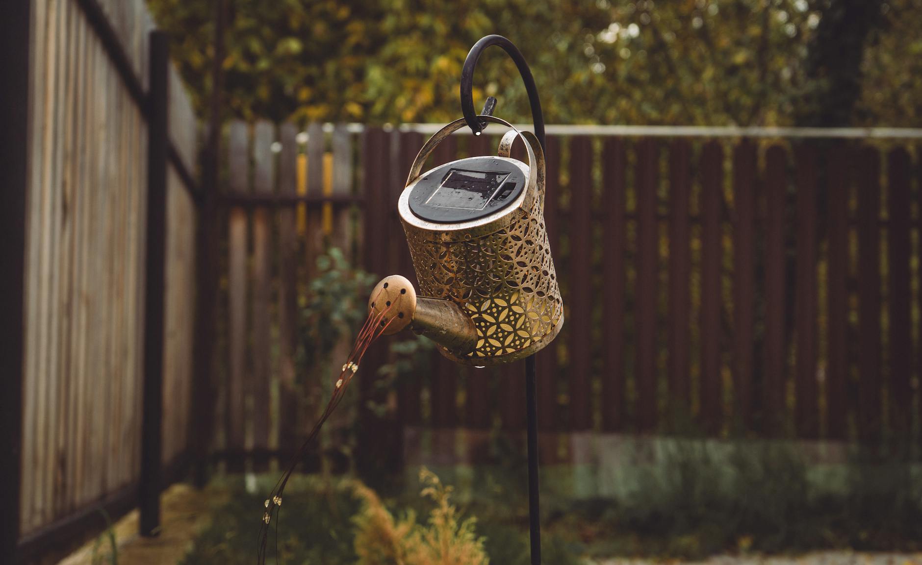 Dekoracyjna konewka solarna świeci w przytulnym ogrodzie z tyłu domu