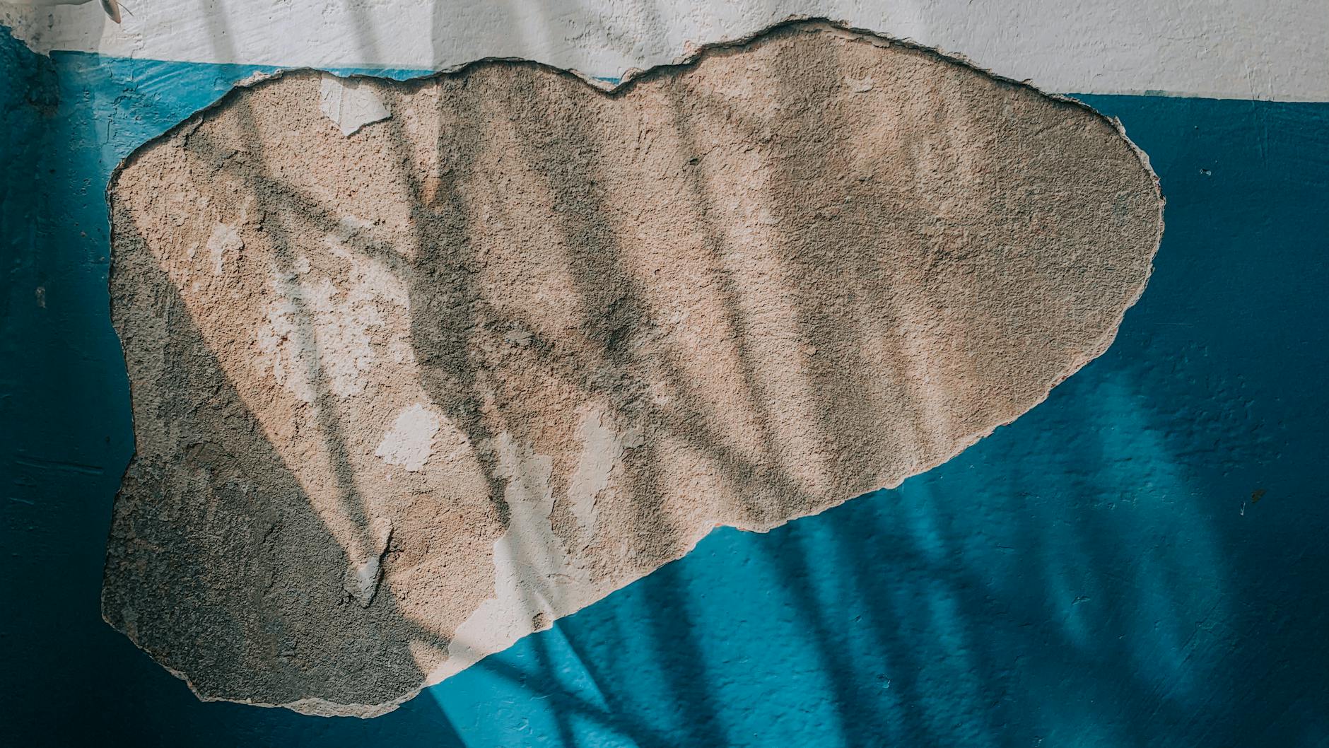 Zbliżenie ściany z łuszczącą się niebieską farbą i odsłoniętym tynkiem