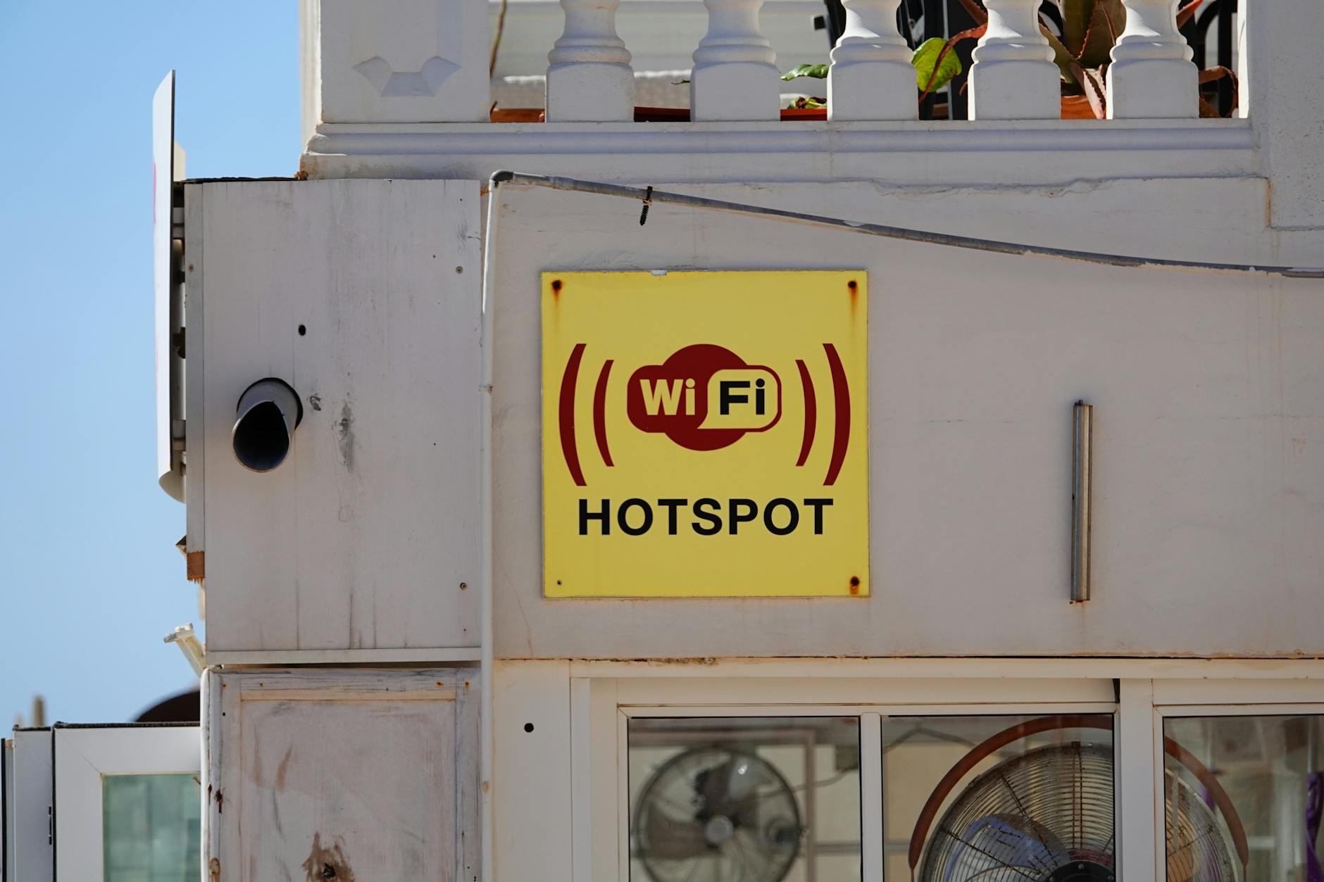 Żółty szyld WiFi hotspot na elewacji budynku, symbol łączności w ogrodzie