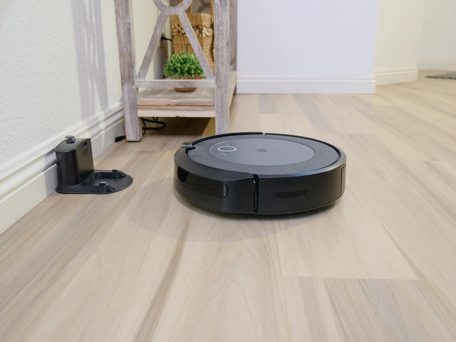 Robot sprzątający na drewnianej podłodze obok stacji dokującej